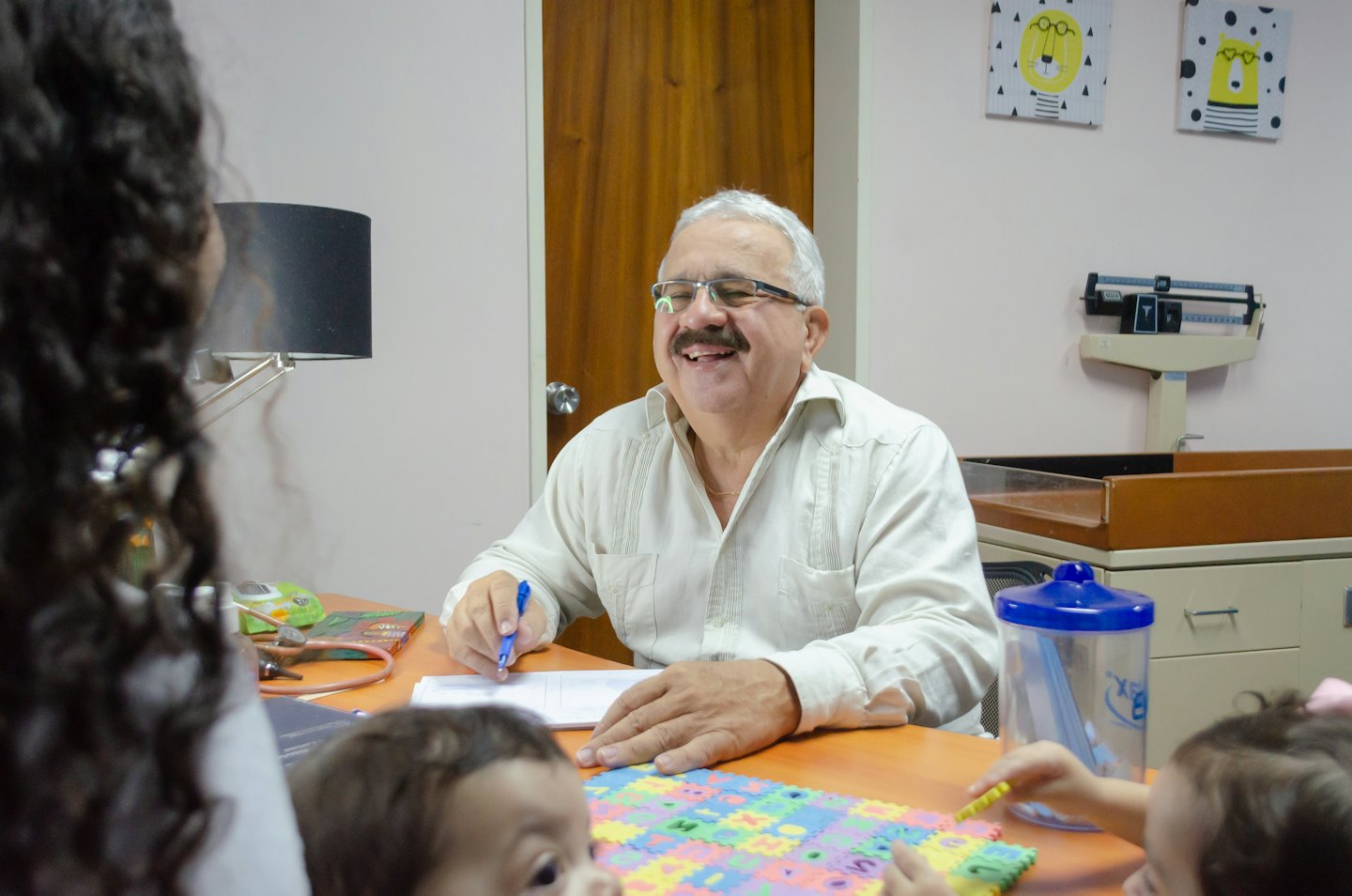 Doctor sits at his desk signing papers in his office.